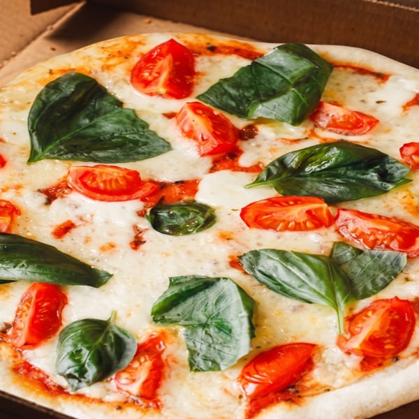 Margherita pizza with melted cheese, sliced tomatoes, and fresh basil in a cardboard box.