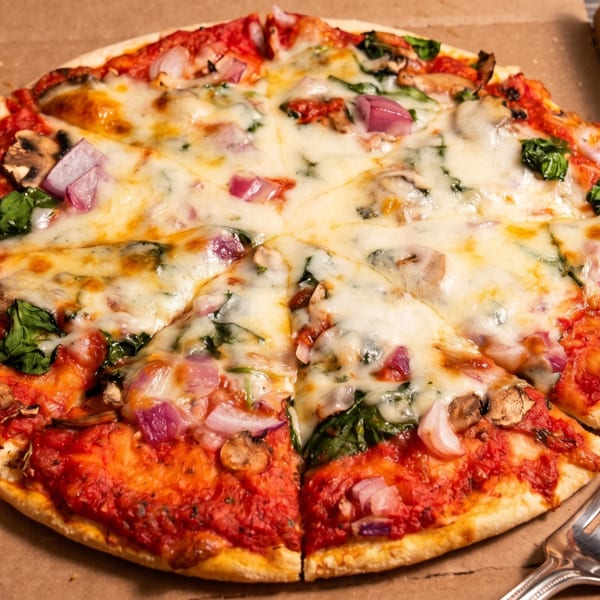 Sliced pizza with cheese, red sauce, spinach, mushrooms, and red onions in a cardboard box with a fork.