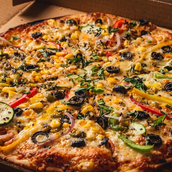 Whole vegetarian pizza with corn, olives, peppers, and zucchini in a cardboard box.
