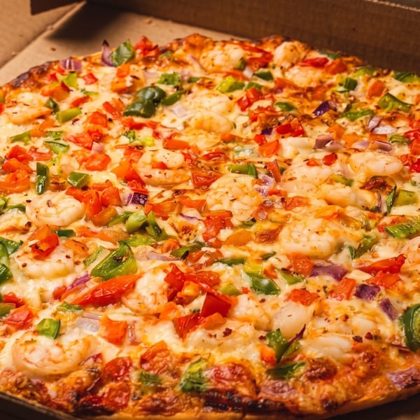 Whole shrimp pizza with tomatoes, green peppers, and red onions in a delivery box.